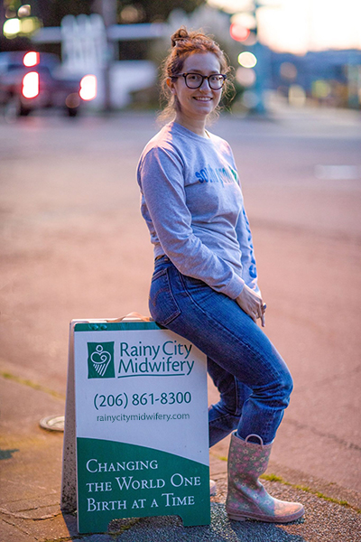 Midwife Sara Alvarado sits on the Rainy City sign after a birth at Center for Birth